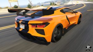 Image de l'arrière du bolide américain Coquette D10. Le véhicule est peint en orange avec deux bandes noires traversant la voiture verticalement. Un gros aileron de course est fixé sur le coffre à l'arrière.