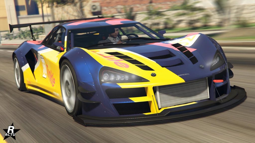 Vue de devant de la supersportive Progen Itali GTB Custom dans le jeu vidéo Grand Theft Auto Online. La voiture est peinte en mauve et avec des touches de jaunes et rouges pour ce qui est de sont motif se nommant "Tinkle"