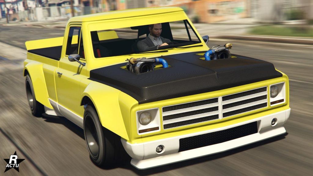 Image d’un pickup Declasse Yosemite Drift de couleur jaune avec un système d’échappement double personnalisé qui sort du capot en carbone, indiquant un moteur modifié en dessous. Le véhicule est représenté en mouvement sur ce qui est une rue urbaine.
