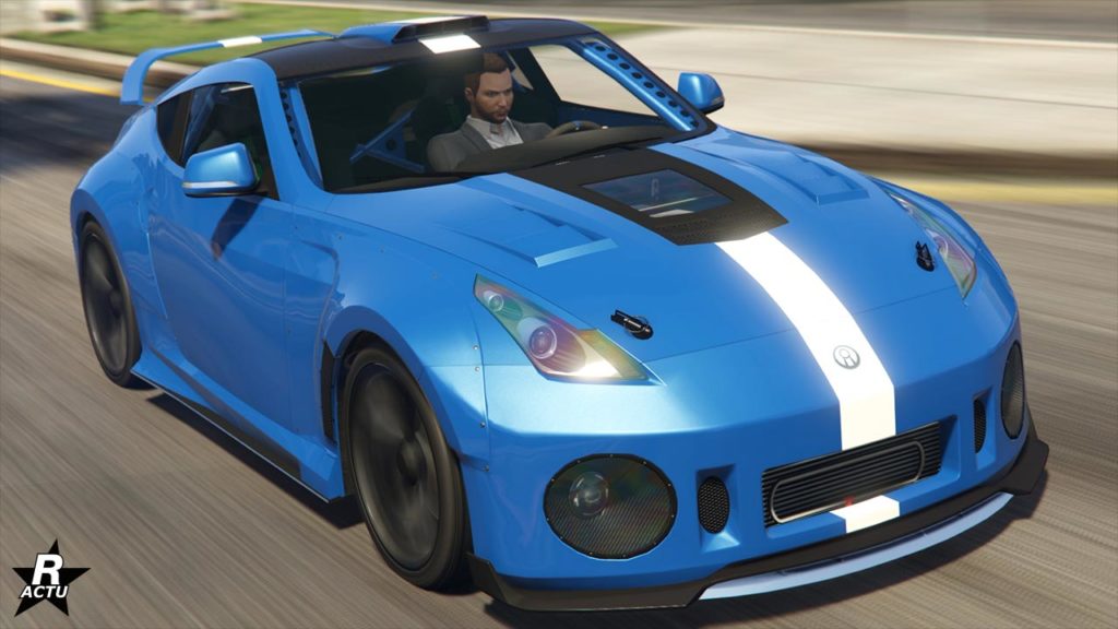 Une voiture Annis Euros de couleur bleue avec une bande blanche au centre, en mouvement dans le jeu vidéo GTA Online. La voiture a un design sportif, avec des phares avant aérodynamiques en verre avec des reflets arc-en-ciel et un pare-chocs avant large. L’intérieur de la voiture est visible mais pas clairement détaillé à cause des reflets sur les vitres.