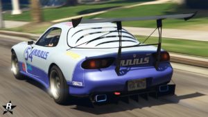 Cette image montre la vue arrière d’une voiture de sport bleue avec le texte ‘ZR350’ sur elle, indiquant le modèle du véhicule dans le jeu GTA Online. La voiture a un grand aileron arrière noir, des bandes de course blanches sur le dessus, et est ornée de divers autocollants et logos de sponsors, dont ‘RON OILS’ et ‘Xero Gas’. La plaque d’immatriculation indique ‘RSG ACTU’. Le véhicule est sur une route avec de la verdure en arrière-plan, suggérant qu’il est en mouvement.