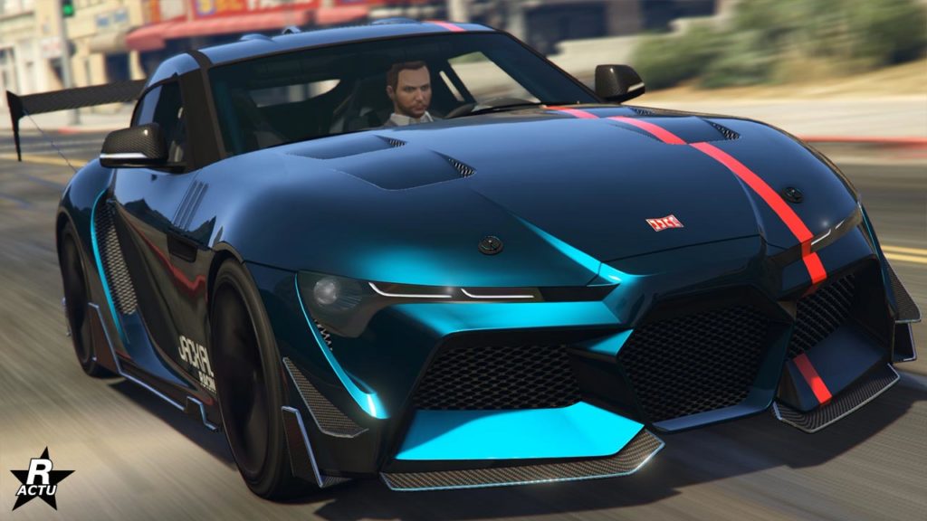 Image d’une voiture de sport moderne avec une finition mate bleu foncé et noire dans le jeu vidéo GTA Online. Des rayures rouges et bleu clair accentuent le design de la voiture, traversant son corps. Le nom de se véhicule est la Jester RR de la marque japonaise Dinka., Il y a quelques inscriptions sur le côté avant. Elle a un design de grille avant agressif avec de grandes prises d’air. La voiture est en mouvement dans une rue de la ville pendant la journée ; des effets de flou de mouvement sont visibles autour des roues et de l’arrière-plan où les bâtiments et structures de la ville sont légèrement flous en raison de la vitesse de la voiture.