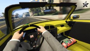 Cette image représente une vue à la première personne de l’intérieur d’une Dinka RT3000 jaune dans le jeu vidéo GTA Online. La main du conducteur est visible, tenant le volant noir qui a divers boutons et le mot ‘DINKA’ écrit dessus. L’intérieur de la voiture est principalement jaune avec des détails noirs et présente un affichage numérique au centre du tableau de bord. Un extincteur rouge est monté sur le sol côté passager. Le rétroviseur offre une réflexion de la scène derrière, et les rétroviseurs latéraux sont également visibles montrant des réflexions. À l’extérieur, il semble faire beau avec un ciel dégagé ; des bâtiments et des palmiers bordent la rue qui s’étend devant.