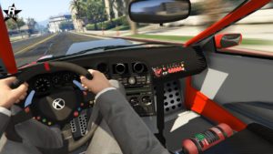 Cette image montre une perspective à la première personne de l’intérieur d’une voiture de courseIl s'agit de la voiture japonaise Karin Calico GTF. Les mains du conducteur sont sur le volant qui a divers boutons et un logo au centre. Le tableau de bord est équipé de plusieurs jauges et interrupteurs, indiquant qu’il est conçu pour la conduite de performance. Un extincteur est monté sur le sol à côté du siège du conducteur, soulignant les précautions de sécurité typiques dans les voitures de course. Le véhicule a un thème intérieur rouge et noir avec des composants métalliques visibles. À l’extérieur du pare-brise, on peut voir une rue bordée de palmiers et de bâtiments sous une lumière du jour éclatante.