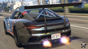 Cette image montre la vue arrière d’une Pfister Comet S2, une voiture de sport dans le jeu vidéo GTA Online, elle est représentée avec beaucoup de détails. La voiture est grise avec des accents noirs, comportant un grand aileron arrière, des tuyaux d’échappement doubles émettant des flammes indiquant l’accélération, et des plaques d’immatriculation personnalisées indiquant “RSG ACTU”. La scène se déroule sur une route urbaine avec des environs flous suggérant une grande vitesse.