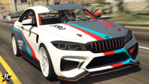 Une voiture de sport blanche Ubermacht Cypher avec des bandes de course bleues, rouges et grises, ainsi que le numéro ‘73’ sur le capot. Le design moderne de la voiture présente des angles vifs, de grandes prises d’air sur le pare-chocs avant, et une marque de sponsors fictifs bien en vue.