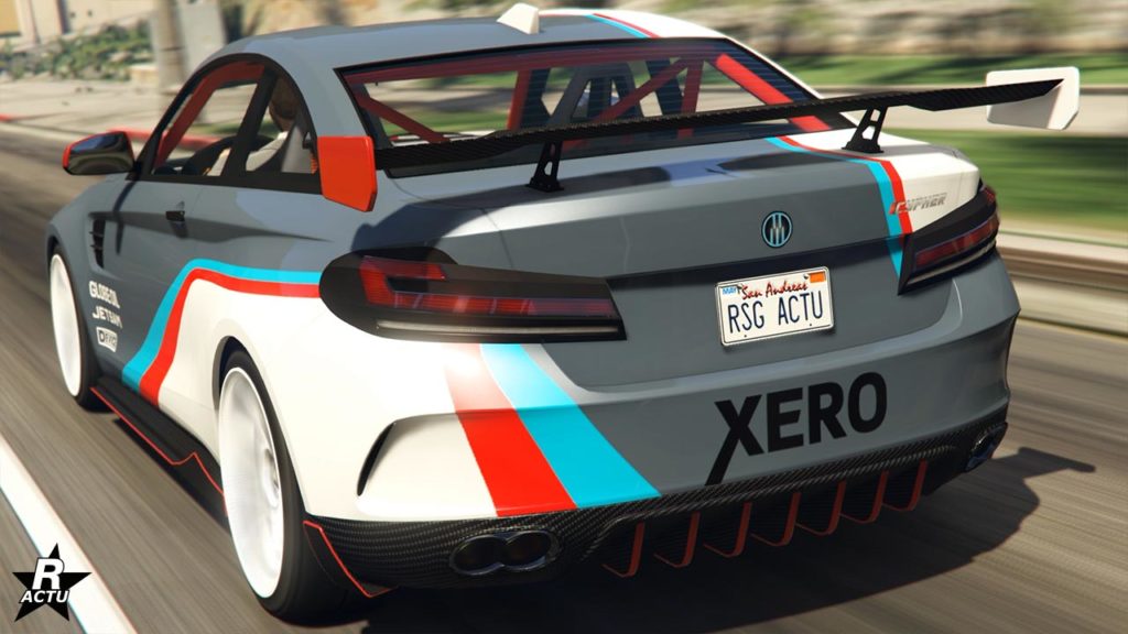 L’image montre la vue arrière d’une voiture de sport blanche Ubermacht Cypher avec un aileron arrière proéminent et des autocollants de course, y compris des bandes en bleu, rouge et gris clair. La plaque d’immatriculation indique ‘RSG ACTU’, et il y a des logos comme ‘XERO’ sur le pare-chocs. L’image a été prise pendant une journée ensoleillée avec un ciel dégagé sur une route dans le jeu vidéo GTA Online.