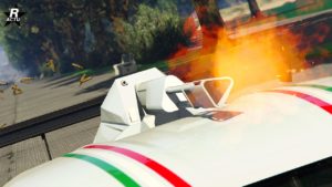 Vue rapprochée d’une Pegassi Ignus armée blanche avec des bandes vertes, blanches et rouges. La voiture est équipée d’un minigun monté sur le toit. L’arme est en action, comme en témoignent les flammes visibles et les douilles éjectées.