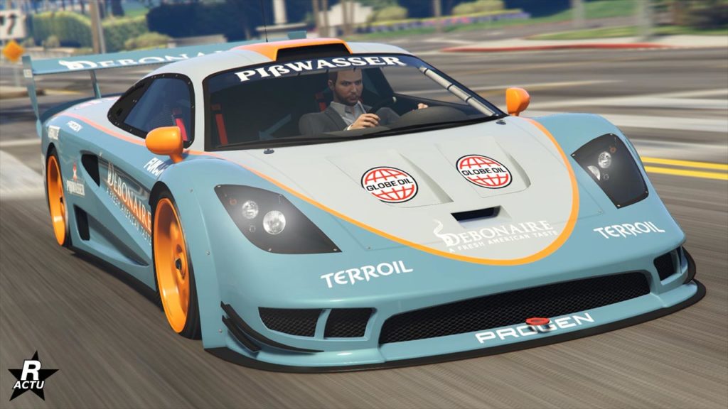 Vue avant d’une voiture de sport bleu clair avec des accents orange, identifiée comme la Progen Tyrus dans le jeu vidéo GTA Online. Le véhicule présente un marquage avec des logos tels que “PISWASSER”, “eCola”, “Terroil”, et d’autres sur le capot et les côtés. La voiture a une carrosserie basse et aérodynamique avec un grand splitter avant, des goupilles de capot de style course, et un pare-brise qui reflète l’environnement environnant. L’arrière-plan dispose d'un flou de mouvement indiquant une grande vitesse de la Tyrus qui circule dans une rue de Los Santos.