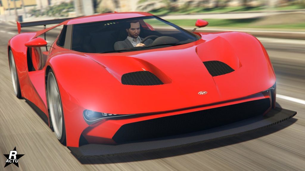 Vue de face d’une voiture de sport Vapid FMJ de couleur rouge vif en mouvement sur une rue de ville dans GTA Online. L'image met en évidence son design aérodynamique qui a de grandes entrées d’air sur le capot et les profils et un aileron arrière distinctif pour la force d’appui.