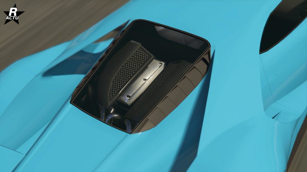 Vue rapprochée du pare-brise arrière d’une voiture Vapid FMJ de couleur bleu vif, qui dispose d’une vitre à travers laquelle le bloc moteur est visible. Le capot du compartiment moteur semble être fait d’un matériau noir.