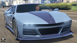 Vue avant d’une Ubermacht SC1 de couleur bleue argentée, qui est une voiture de sport de luxe dans le jeu vidéo GTA Online. La voiture est représentée sous un angle avant, mettant en valeur son design élégant avec des lignes nettes, de grandes prises d’air sur le pare-chocs avant, et des phares étroits distinctifs. Le logo Ubermacht est visible sur le bas du capot.