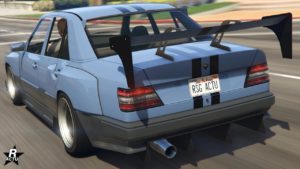 Vue arrière du véhicule Benefactor Vorschlaghammer dans GTA Online. C'est une berline peinte en un gris bleuté sur le haut de la voiture, tandis que sur le bas, elle est gris anthracite. Elle a également des ailes arrière larges sur les côtés.
