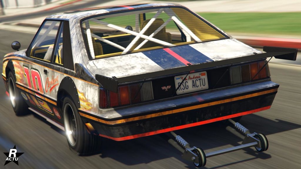 Vue arrière de la voiture de type grosse cylindrée "Vapid Dominator FX" dans GTA Online. Il s'agit d'un véhicule américain des années 1980 de couleur blanche avec des motifs de flammes à l'avant. À l'arrière du véhicule, des roulettes s'y trouvent pour maintenir la voiture sur la route lors de courses de dragsters. La sortie du pot d'échappement se fait sur les côtés latérales du pare-chocs arrière.