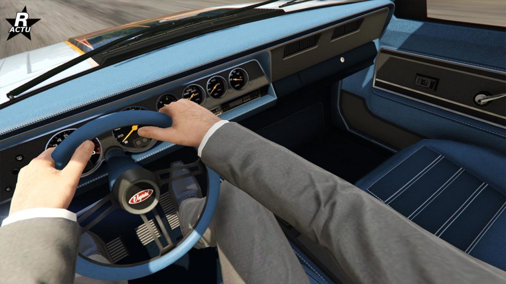 Vue du point de vue du conducteur de la voiture Vapid Dominator FX dans GTA Online. Le tableau de bard est typique des années 1980, différents conteurs analogique s'y trouve. L'habitacle est recouvert par un tissu bleu ciel.