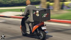 Vue arrière de la moto Pegassi Pizza Boy. La peinture de la moto est orange et une sacoche de transport de pizza se trouve à l'arrière avec l'inscription "Pizza This..." aux couleurs du drapeau italien.
