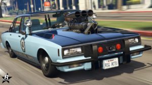 Vue avant de la voiture de police Declasse Impaler LX Cruiser dans le jeu vidéo GTA Online. La voiture est de couleur bleue ciel sur la partie inférieure du véhicule, tandis que le capot, le toit et le coffre sont bleu foncé. Le bloc moteur ressort du capot à son centre. Un gros gyrophare rouge est allumé sur le toit de la Declasse Impaler LX Cruiser.