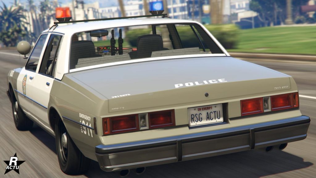 La Declasse Impaler LX Cruiser vue de derrière. Il s'agit d'un véhicule de flic dans le jeu vidéo Grand Theft Auto Online du studio Rockstar Games. Il s'agit d'une voiture des années 1980 de couleur gris et blanc. La carrosserie porte les inscriptions "police", "911" ou encore le logo du LSPD. Les gyrophares sur le toit son allumés.