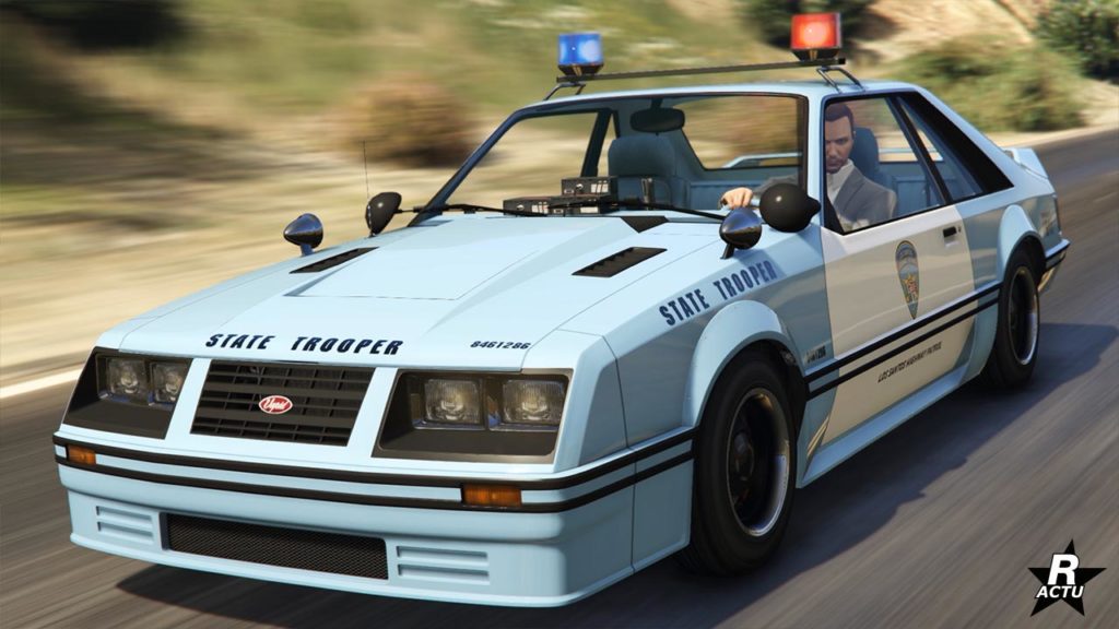 Vue avant de la voiture de police Vapid Dominator FX Interceptor qui s'inspire d'une Ford Mustang de troisième génération. Le véhicule est intégralement de couleur bleu ciel à l'exception des portières qui sont blanches avec le logo de police d'État de San Andreas. Les inscriptions "State Trooper" sont visibles à différents emplacements sur la carrosserie. Un double gyrophare des années 1980 se trouve sur le toit, il est allumé.