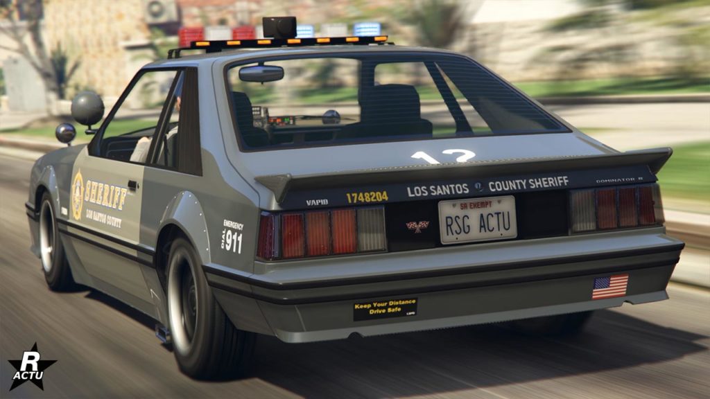 La bagnole de police Vapid Dominator FX Interceptor dans le jeu vidéo Grand Theft Auto Online. La voiture est vue de l'arrière, elle est de couleur gris et beige avec un petit aileront sur le coffre et des gyrophares allumés sur le toit.