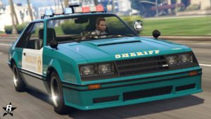 Image avant de la voiture Vapid Dominator FX Interceptor dans GTA Online. Il s'agit d'un véhicule de police apparentée au shérif comme l'indique les inscriptions "Sheriff" sur la carrosserie. Le véhicule est de couleur vert, et blanc pour ses portes. Les gyrophares sur les toits sont actifs.