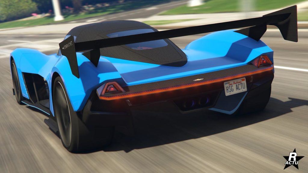 Vue arrière d’une voiture de sport Dewbauchee Vagner bleu vif du jeu vidéo GTA Online en mouvement sur une route de Los Santos. La voiture présente un aileron arrière noir proéminent, des feux arrière distinctifs et des tuyaux d’échappement doubles. Il y a une plaque d’immatriculation qui indique ‘RSG ACTU’.