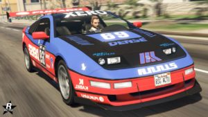 L’image montre une vue frontale d’une voiture du jeu vidéo GTA Online, il s'agit du coupé Annis Euros X32. La voiture est principalement mauve avec des accents rouges et blancs, comportant divers logos de sponsors fictifs et le numéro ‘69’ sur son capot en carbone. Le design rappelle les voitures de sport utilisées dans les courses professionnelles.