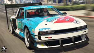 L’image montre une vue frontale d’une voiture de course stylisée provenant du jeu vidéo GTA Online. La voiture a une livrée élaborée avec divers graphiques, y compris des noms de marques fictives de la saga Grand Theft Auto comme “Tenshun” ou 'Junk' qui sont affichés sur le capot. Il y a aussi la marque “The Disruption” écrit sur le pare-soleil. Le véhicule est équipé d’un grand aileron arrière, indiquant qu’il est conçu pour la stabilité à haute vitesse.