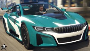 L’image montre une voiture Ubermacht Niobe vert pétrole provenant du jeu vidéo GTA Online. La vue est prise de l’avant, mettant en évidence le design élégant du véhicule avec des phares distinctifs, une grande calandre chromée et un pare-chocs agressif. Le capot présente une ouverture noire, et en arrière-plan, on distingue un paysage urbain flou, indiquant le mouvement.