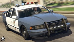 La voiture de police Declasse Impaler SZ Cruiser vue de devant dans le jeu GTA Online. Elle est peinte en duochrome blanc et gris. Un pare-buffle avant se trouve accroché au pare-chocs