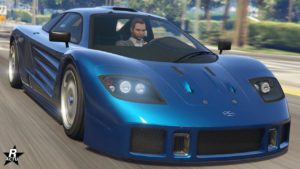 Vue avant de la voiture de sport Progen GP1 des années 90/2000. La carrosserie du véhicule est peinte en bleu et la voiture roule dans une rue ensoleillée de Los Santos dans le jeu GTA Online