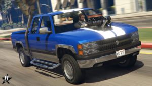 Image vue de devant du véhicule tout-terrain Declasse Yosemite 1500 dans le jeu vidéo GTA Online. La voiture est peinte en bleu et ses extrémités (bas de caisse, pare-chocs...) sont chromés. Deux bandes blanche traversent verticalement la voiture du constructeur américain Declasse. Sur le capot, une partie du bloc moteur ressort et est visible.