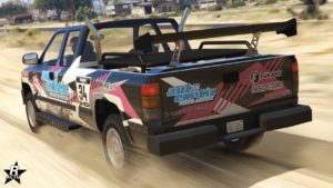 Vue arrière du tout-terrain Declasse Yosemite 1500 circulant sur un chemin de sable dans le Grand Senora Desert. La voiture de GTA Online est de couleur noire et a le motif "Auto Exotic" équipé sur sa carrosserie. Un grand aileron en carbone est fixé à l'arrière du plateau du véhicule.