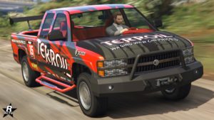 La voiture Declasse Yosemite 1500 dans le jeu GTA Online vue de devant. Le véhicule est peint en rouge et a le motif "Course Terroil" appliqué sur sa carrosserie. Le véhicule circule sur un chemin en terre dans une forêt.