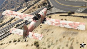 Vue arrière et du dessus de l'avion Western Duster 300-H dans le jeu vidéo GTA Online. Le véhicule dispose d'un motif militaire duochrome blanc et rose.