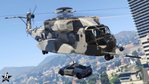Image de l'avant de l'hélicoptère lourd Buckingham DH-7 Iron Mule dans le jeu vidéo GTA Online. Le véhicule dispose d'un camouflage militaire duochrome noir et gris, l'hélicoptère porte par son crochet la voiture de police Coquette D10 de poursuite
