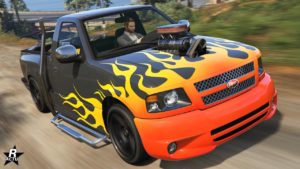 Vue avant de la voiture tout-terrain Vapid Firebolt ASP dans le jeu vidéo GTA Online. Le véhicule est peint en gris, à son bloc moteur qui dépasse de son capot et une décalcomanie de flammes rouges et jaunes sont présentes à l'avant de la voiture.