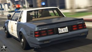 Image arrière de la voiture de flic Willard Faction de proximité dans GTA Online. Elle est peinte en banc et gris, s'est gyrophares circulaires sont allumés et un petit aileron en forme de bac de canard se trouve sur le coffre.