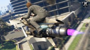L'arrière de la Pegassi Oppressor Mk II dans GTA Online. La moto volante est en vol au-dessus de Los Santos dans le jeu GTA Online. Le réacteur à réaction qui permet de faire léviter le véhicule dans les airs est visible et crache une flamme bleue. La carrosserie dispose d'une décalcomanie militaire de désert aux formes géométriques.