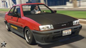 Vue avant de la Karin Futo, la voiture de GTA Online est peinte en rouge vif, et en gris pour les bas de caisse et les pare-chocs. Son capot est intégralement en carbone, tandis que sur le bas de caisse, la décalcomanie jaune typique du véhicule dans les autres Grand Theft Auto est présente.