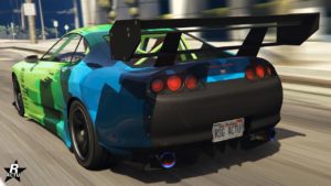 L'arrière du véhicule asiatique Dinka Jester Classique dans le jeu GTA Online. La voiture dispose d'une peinture verte tandis que l'arrière est recouvert par des motifs géométriques de diverses nuances de bleues. Le bas du coffre est en fibres de carbone, ainsi que son grand aileron de course.