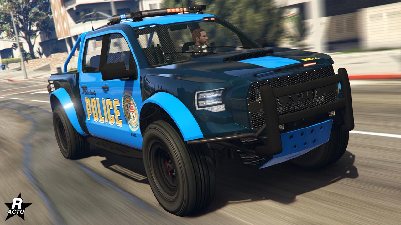 Vue avant de la voiture Vapid Caracara de poursuite qui est conduite dans une rue de GTA Online. Cette voiture de flics dispose de gyrophares sur son toit qui sont allumés. Sa carrosserie est peinte avec un duo de bleus, bleu foncé pour une grande partie de la carrosserie, et en bleu clair pour ses portières et son toit. Le logo de la ville de Los Santos est adossé à côté de l'inscription "police" en jaune sur les côtés latéraux du véhicule tout-terrain.