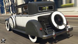 Image de l'arrière du véhicule de GTA Online, Albany Roosevelt Valor. La voiture dispose d'une peinture duochrome blanche et grise, une roue de secours est accrochée à l'arrière, devant une malle.