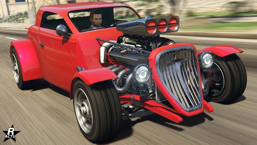L'avant du véhicule de type Hot Road Vapid Hotknife sur une route de GTA Online. La carrosserie de la voiture est entièrement peinte en rouge. Le compartiment du bloc moteur est totalement ouvert et est visible sur l'image, laissant apparaitre le moteur avec son turbocompresseur et ses pots d'échappements latéraux.