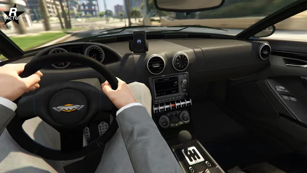 Point du vue du conducteur lors du pilotage de la voiture de sport Rapid GT sur une route de GTA Online. Sur le volant se trouve le logo du constructeur "Dewbauchee" et un petit écran LCD se situe dans la console centrale.