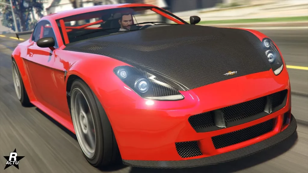 L'avant de la voiture de sport anglaise Dewbauchee Rapid GT, roulant à vie allure dans une rue ensoleillée du jeu vidéo GTA Online. La carrosserie du bolide est peinte en rouge vif et son capot est en carbone, ainsi que son splitter sur le pare-chocs. Dans l'habitable intérieur se trouve une cage d'arceaux de sécurité de la même couleur que le reste du véhicule.