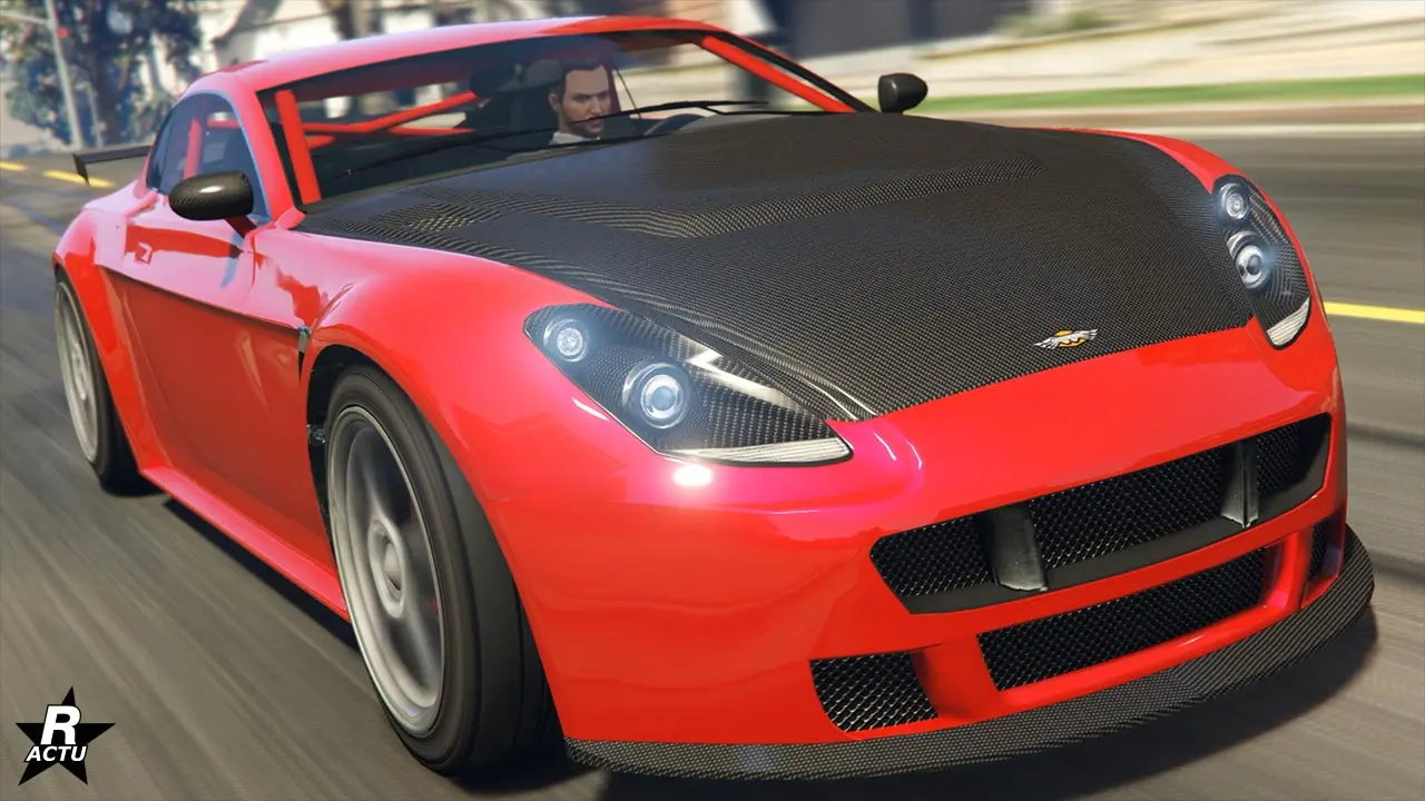 L'avant de la voiture de sport anglaise Dewbauchee Rapid GT, roulant à vie allure dans une rue ensoleillée du jeu vidéo GTA Online. La carrosserie du bolide est peinte en rouge vif et son capot est en carbone, ainsi que son splitter sur le pare-chocs. Dans l'habitable intérieur se trouve une cage d'arceaux de sécurité de la même couleur que le reste du véhicule.