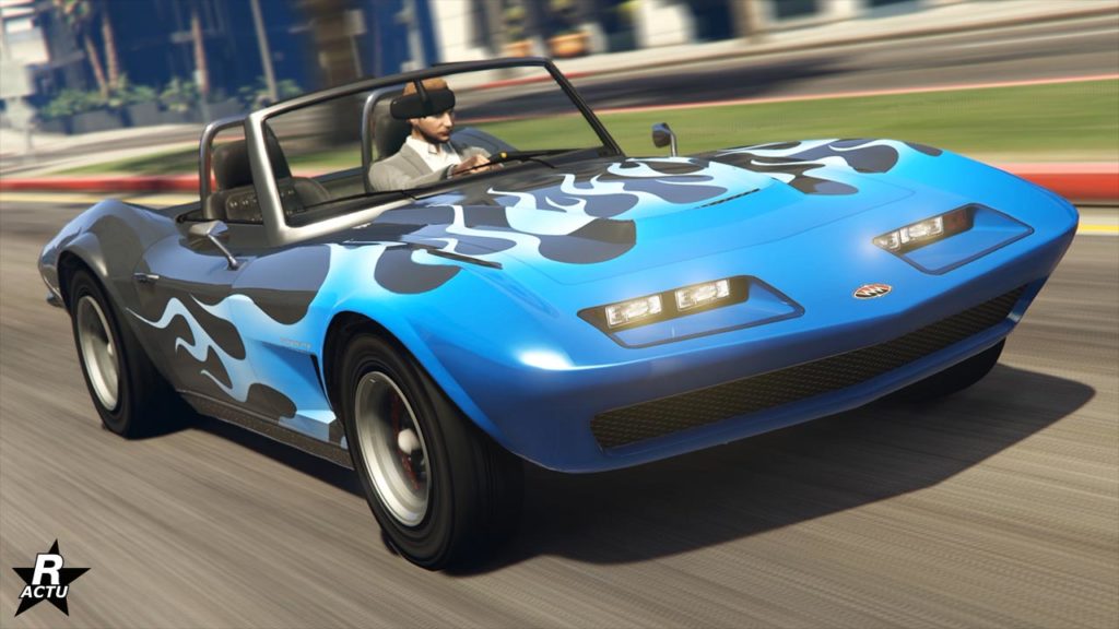Image présentant la voiture Invetero Coquette classique avec une vue avant dans GTA Online. Le bolide est dans sa version décapotable, sa carrosserie est grise anthracite et possède une décalcomanie de flammes bleues sur le capot et l'avant des ailes latérales.