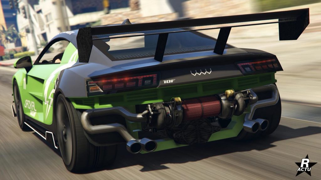 Face arrière de la voiture de sport Obey 10F sur une route du jeu vidéo GTA Online. Le pare-chocs arrière a totalement été retiré et laisse apparaître les pots d'échappements qui sont reliés à un turbocompresseur. Un grand aileron Motorsport se trouve juste au-dessus.