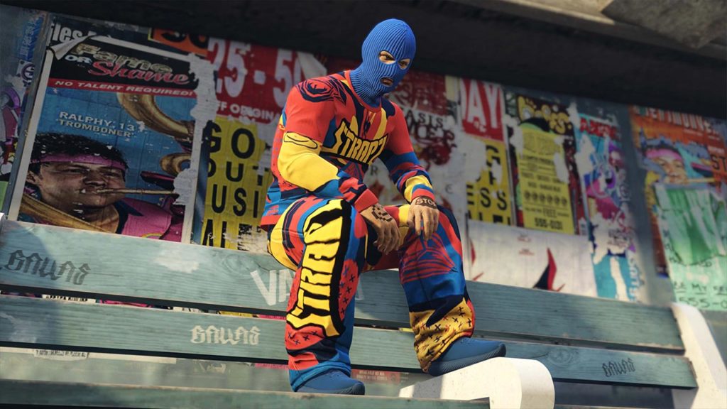 Un personnage jouable de GTA Online avec les vêtements jean et pull Strapz à motifs qui sont exclusifs à l'abonnement GTA+ du juin 2025.